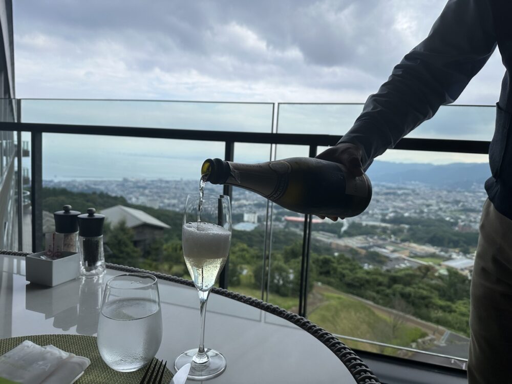 ランチでシャンパンを注いでもらう様子と別府湾の眺め