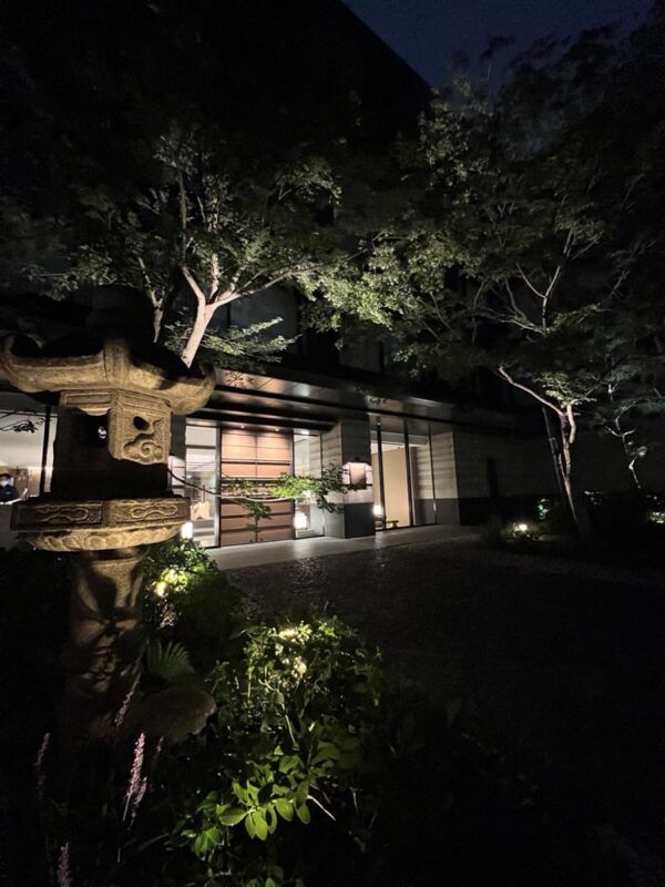 夜の中庭。石灯籠とライトアップされた木、奥に館内の明かり
