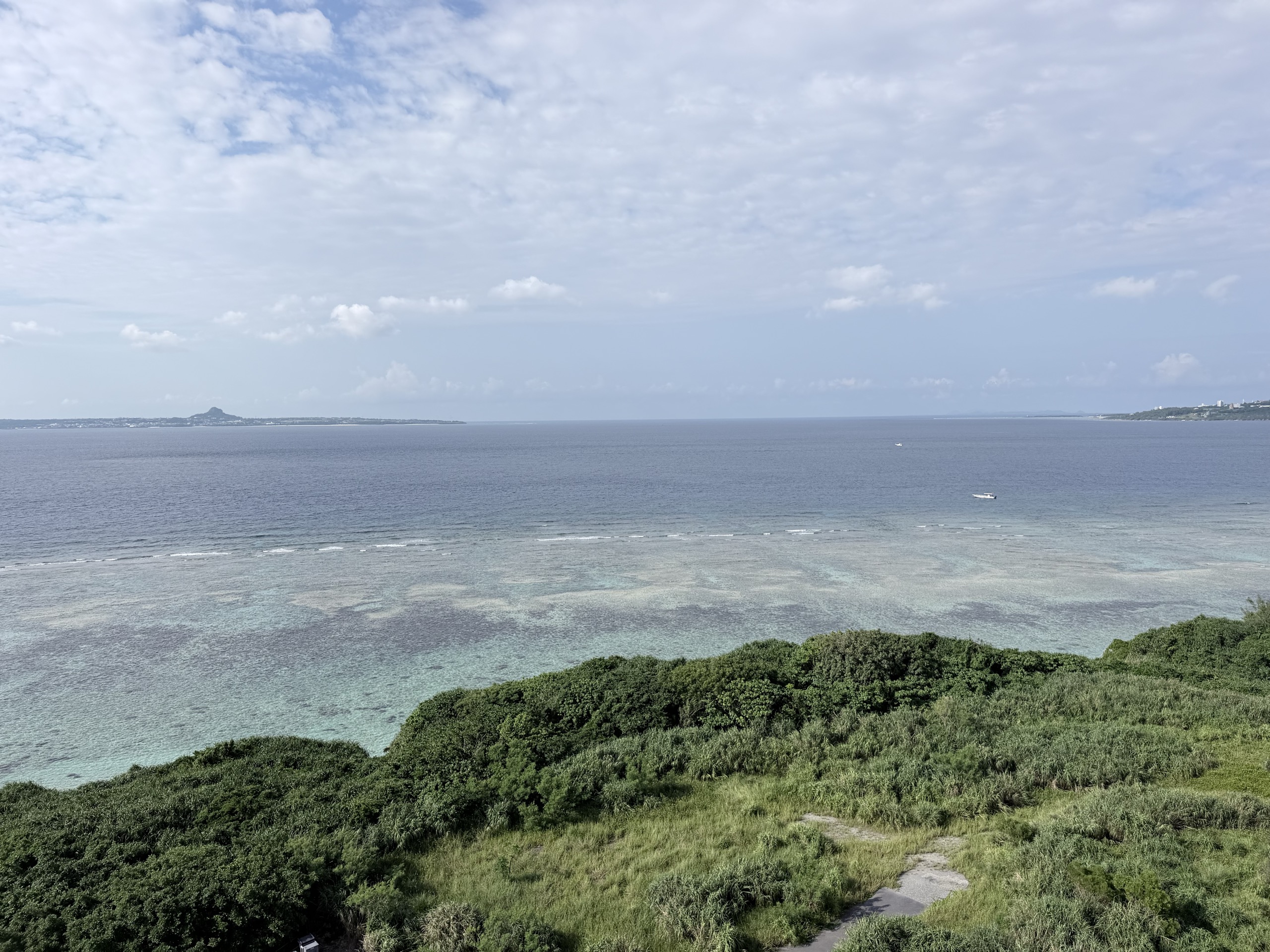 窓の外、遠くに島影と白い小さな船が浮かぶ海