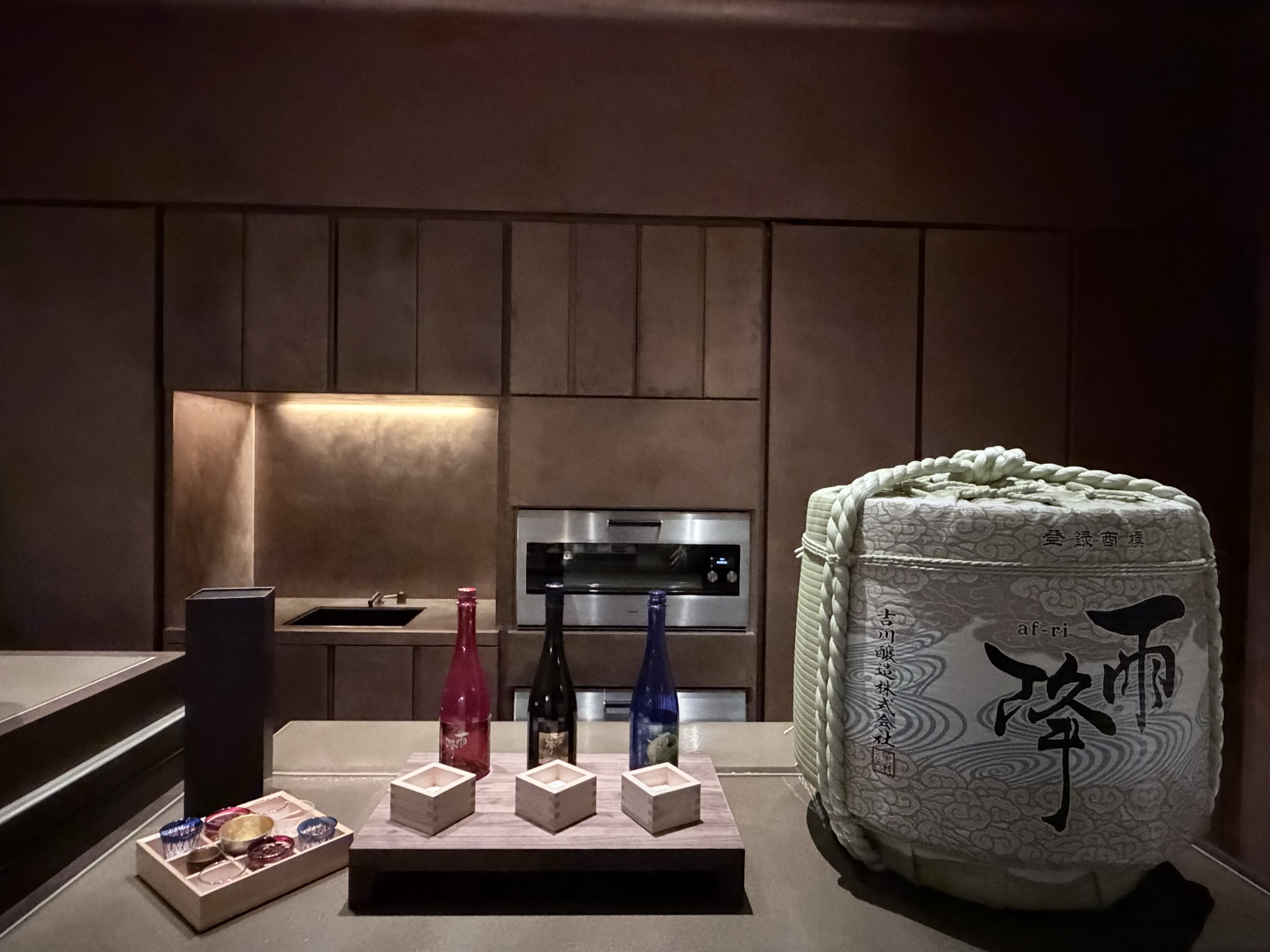 「雨降 af-ri」の文字の酒樽と、日本酒の瓶、お猪口の木箱